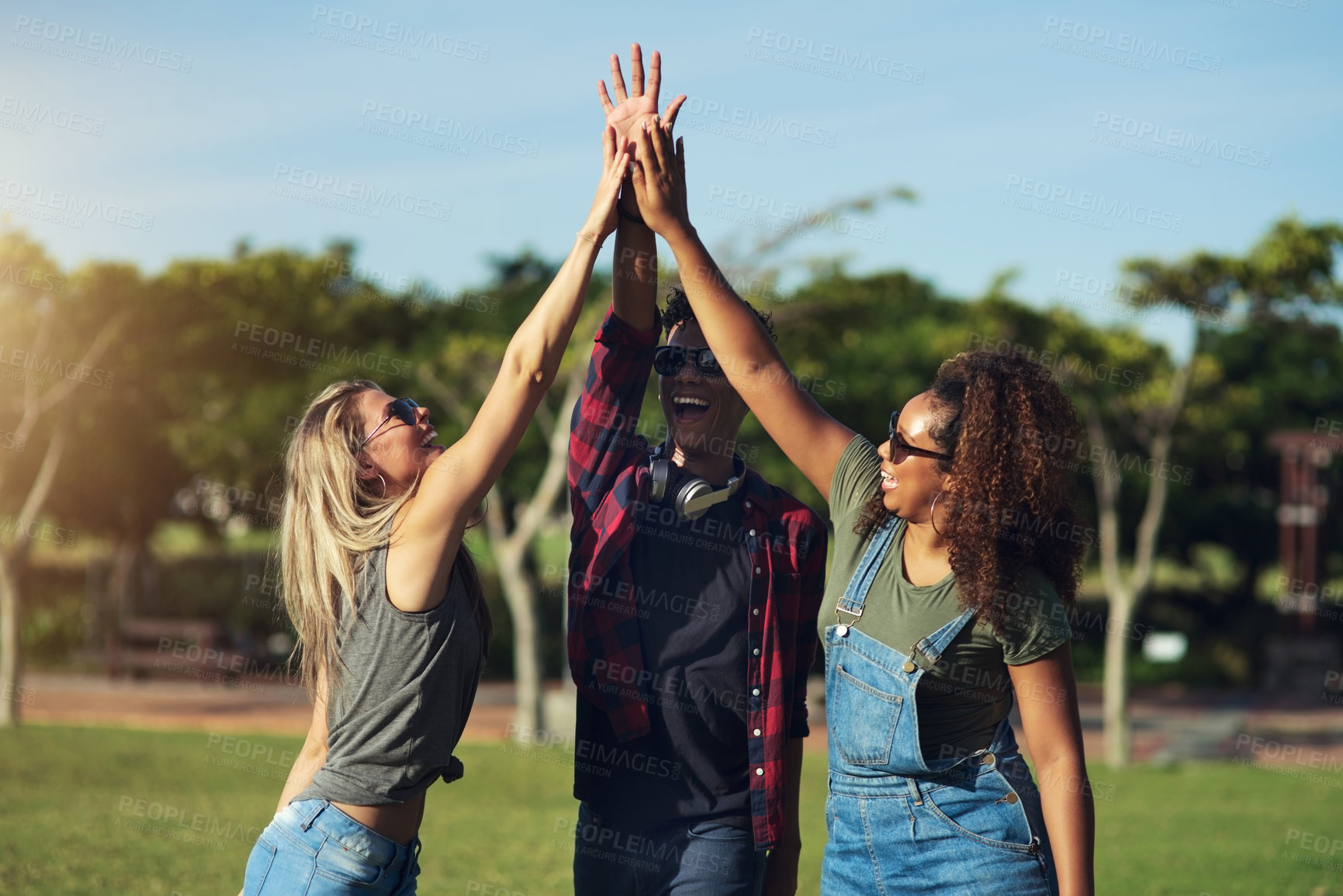 Buy stock photo Shot of a group of cheerful young friends giving each other high fives outside in a park