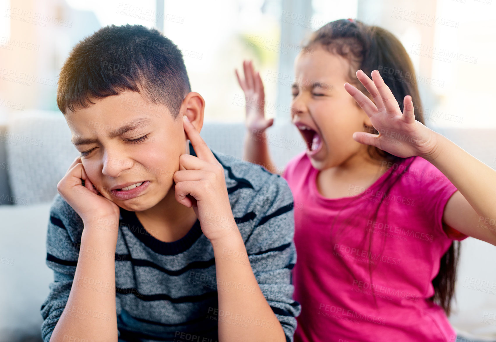 Buy stock photo Shot of a little girl screaming in her big brother's ears while playing in the living room at home