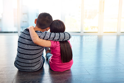 Buy stock photo Rearview shot of two young children sitting on the floor and posing with their arms around each other at home