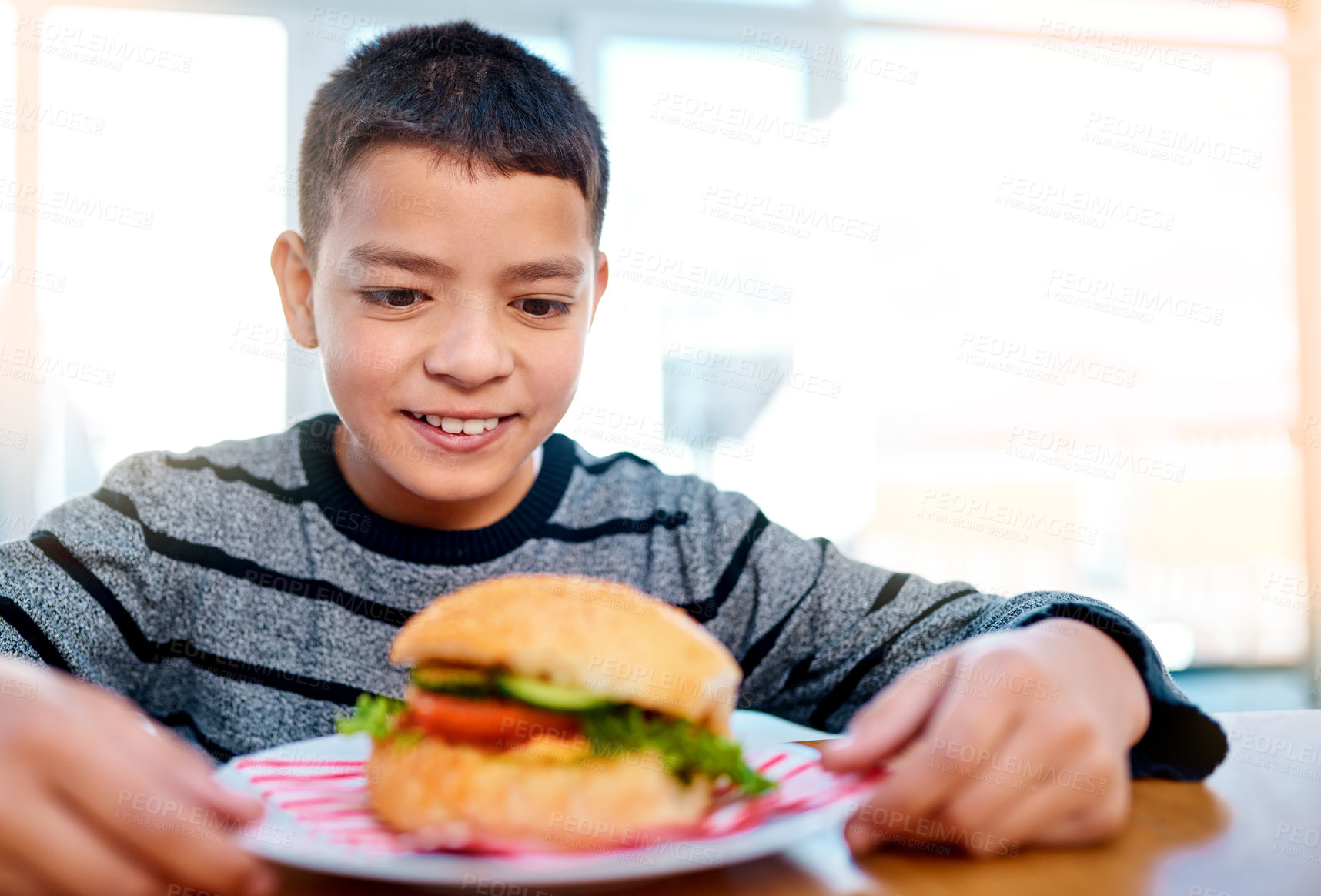 Buy stock photo Shot of a young boy looking at his delicious burger while sitting at his table at home