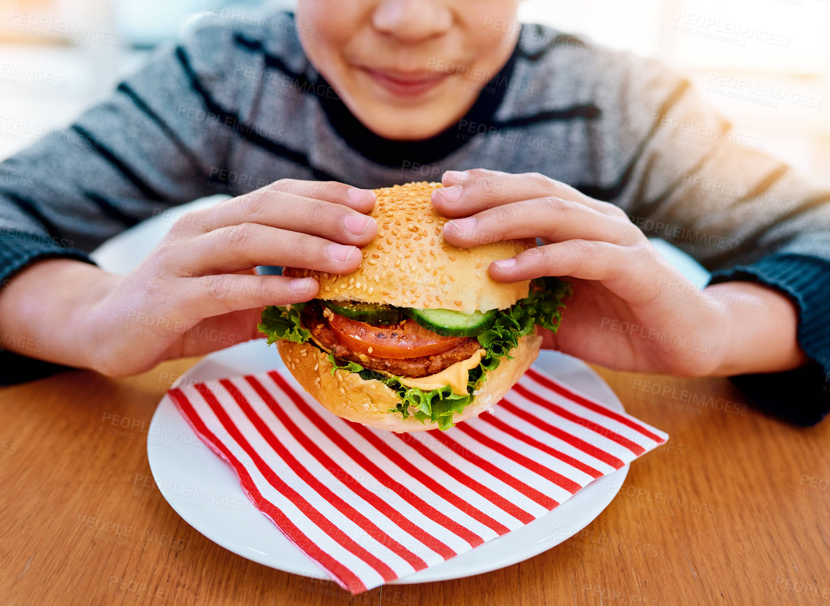 Buy stock photo Child, hands and eating burger on table for delicious lunch, meal or food with healthy vegetables at home. Hand of hungry little boy holding beef hamburger for fresh dinner, nutrition or vitamins