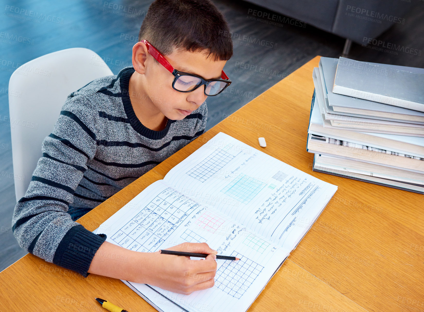 Buy stock photo Boy, student and writing in book for math, studying or homework for learning, assessment or education on table. Smart kid, young child and busy reading mathematics textbook, problem solving and focus