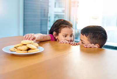 Buy stock photo Shot of two mischievous young children stealing cookies on the kitchen table at home
