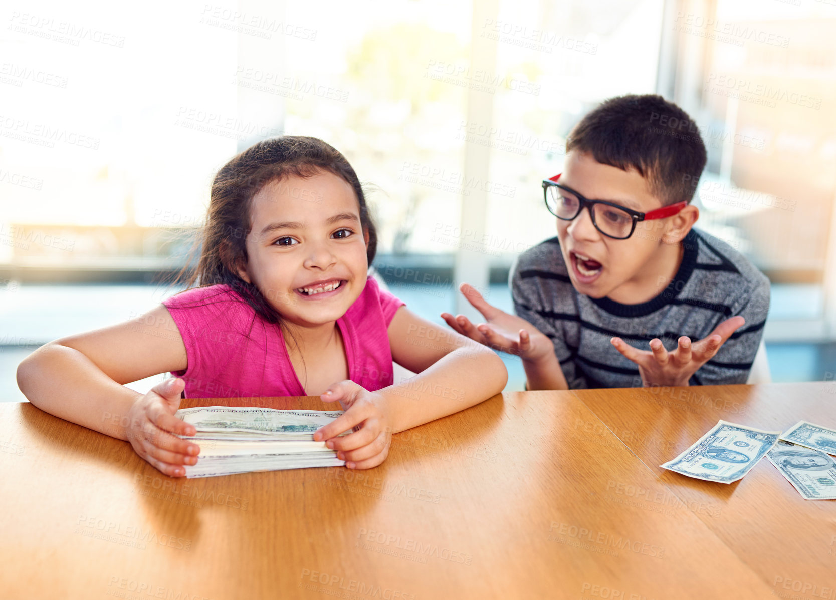 Buy stock photo Children, money and cash for savings in home with conflict, jealousy and frustrated by table. Girl, boy and argument with finance at desk with stack for winner, prize reward and financial payout