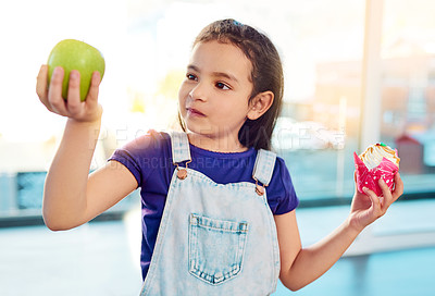 Buy stock photo Shot of an adorable little girl choosing between having an apple or a cupcake as a snack at home