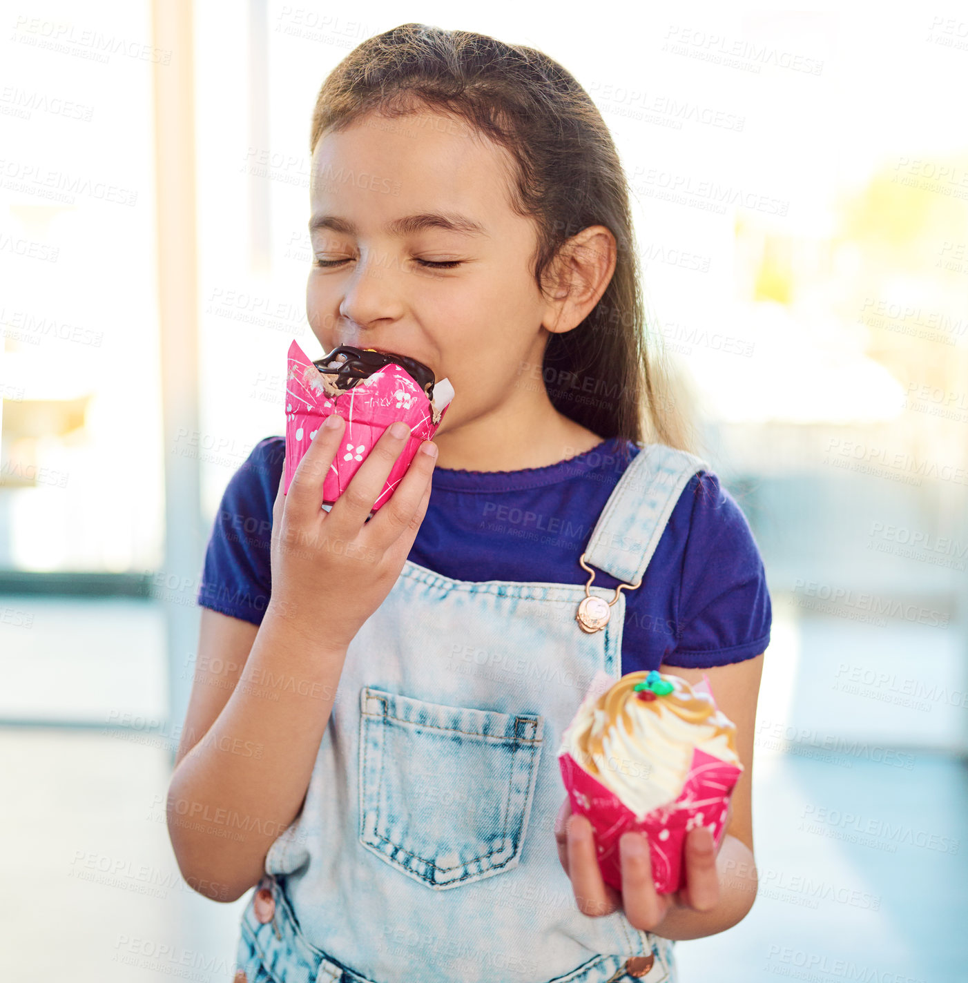 Buy stock photo Shot of an adorable little girl eating a delicious cupcake at home