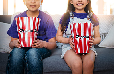 Buy stock photo Shot of two unrecognizable young children sitting on a sofa and eating popcorn while watching movies at home