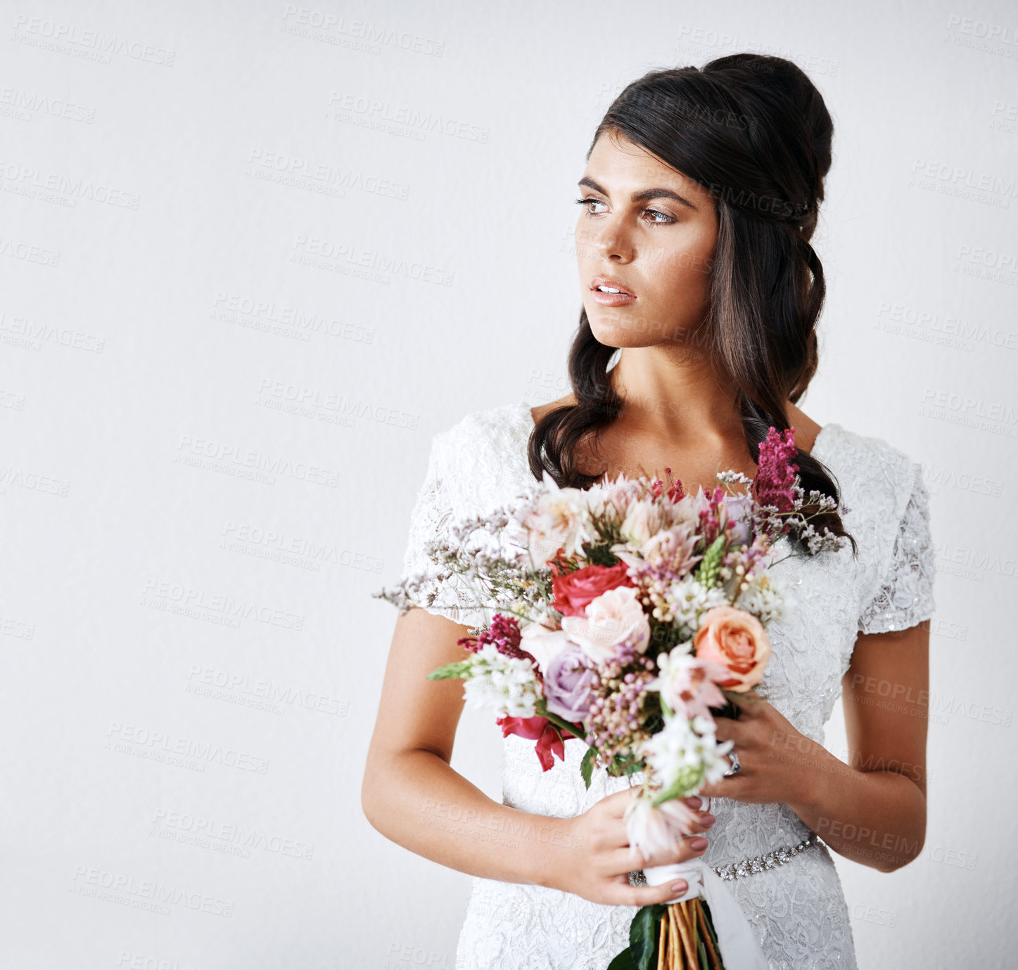 Buy stock photo Studio portrait of a young bride holding a bunch of flowers against a gray background