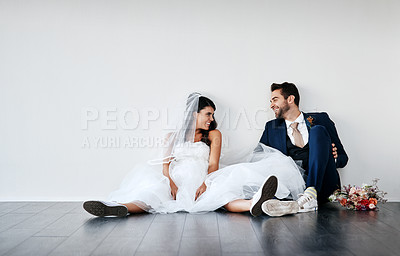 Buy stock photo Studio shot of a newly married young couple sitting together on the floor against a gray background