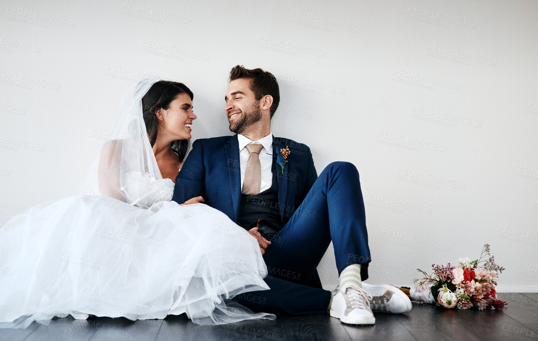Buy stock photo Studio shot of a newly married young couple sitting together on the floor against a gray background