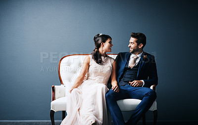Buy stock photo Studio shot of a newly married young couple sitting together on a couch against a gray background
