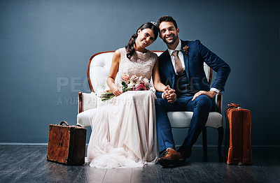 Buy stock photo Studio shot of a newly married young couple sitting together on a couch against a gray background