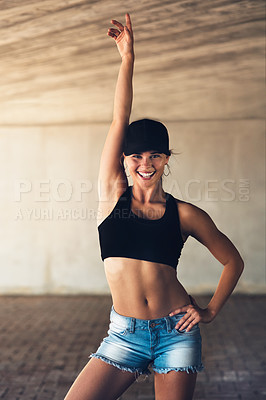 Buy stock photo Shot of an attractive young female street dancer posing with her arm raised while practising out in the city