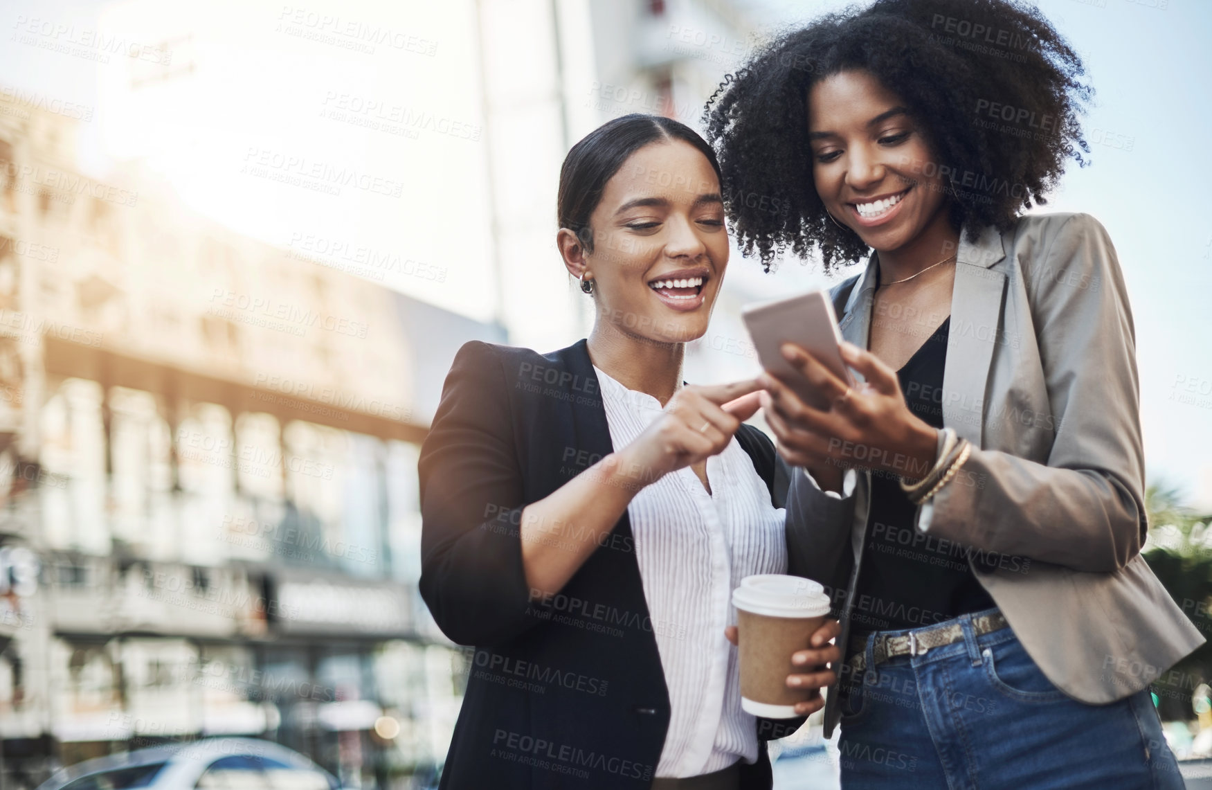 Buy stock photo Shot of two businesswomen looking at something on a cellphone in the city