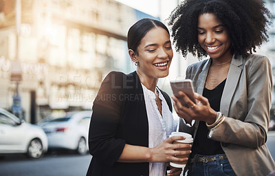 Buy stock photo Shot of two businesswomen looking at something on a cellphone in the city