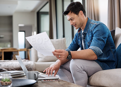 Buy stock photo Shot of a young man using a laptop and going over paperwork at home