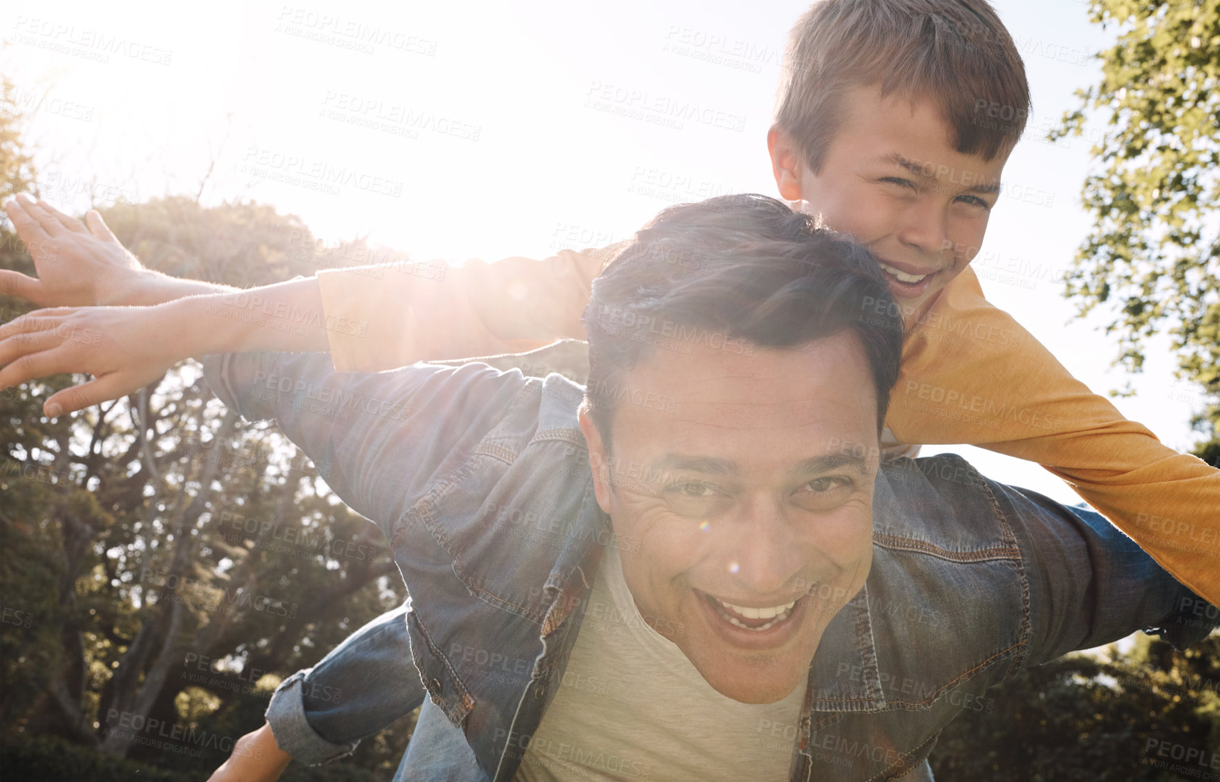 Buy stock photo Shot of a happy father and son enjoying a piggyback ride outdoors