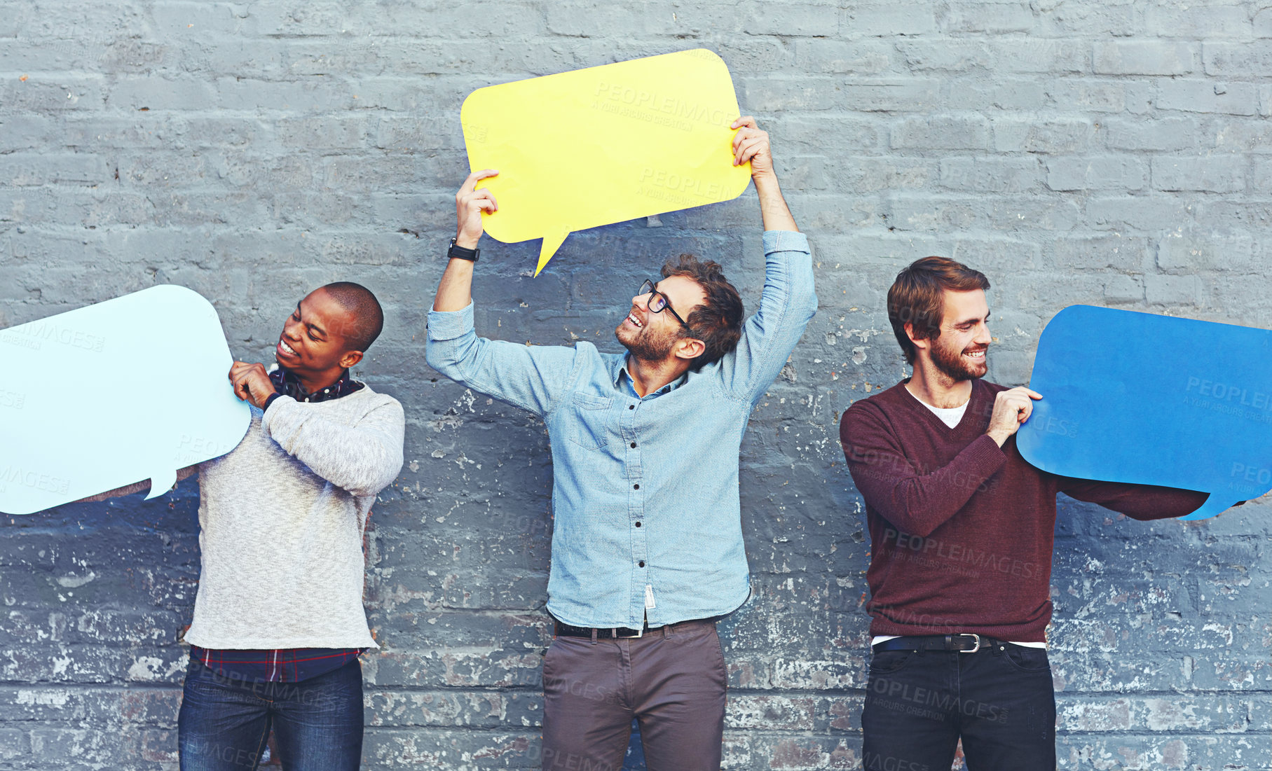 Buy stock photo Shot of a group of young men holding speech bubbles against a brick wall