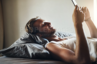 Buy stock photo Shot of a handsome young man using his cellphone while relaxing bed at home