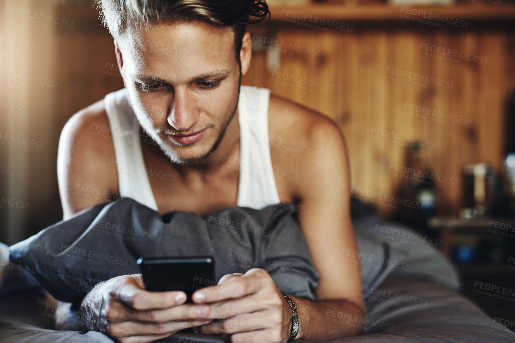Buy stock photo Shot of a handsome young man using his cellphone while relaxing bed at home