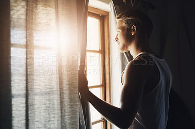 Buy stock photo Shot of a handsome young man looking out of a window in his home