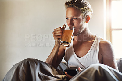 Buy stock photo Shot of a handsome young man using his cellphone while enjoying his morning tea in bed at home