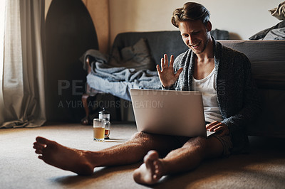 Buy stock photo Shot of a young man making a video call on his laptop while sitting on the floor at home