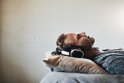 Buy stock photo Shot of a handsome young man listening to music on his headphones while relaxing in bed at home