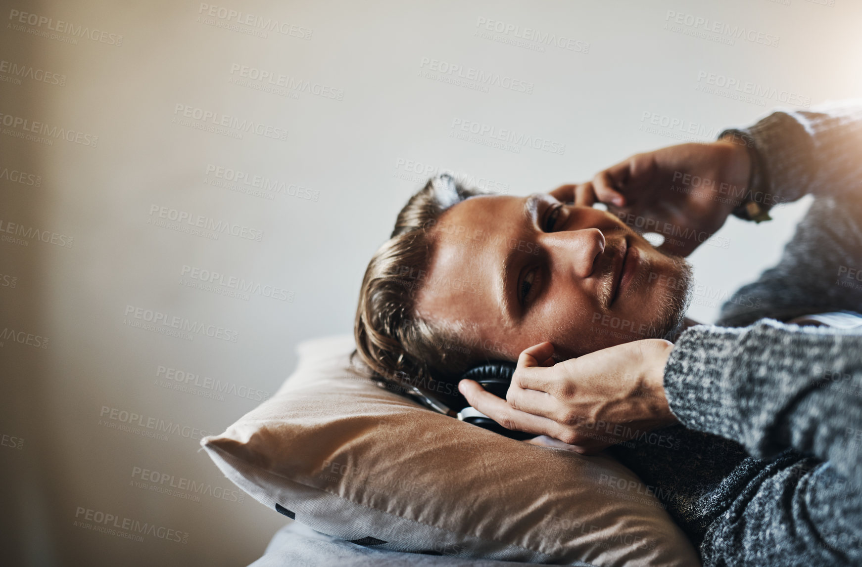 Buy stock photo Shot of a handsome young man listening to music on his headphones while relaxing in bed at home
