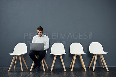 Buy stock photo Full length shot of a handsome young man using a laptop while waiting in line for a job interview