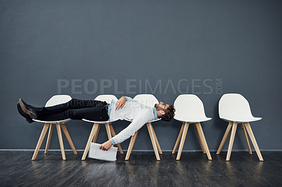 Buy stock photo Full length shot of a handsome young man lying down on a row of chairs while waiting in line for a job interview