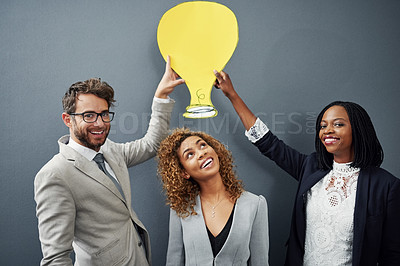 Buy stock photo Studio portrait of three businesspeople standing against a gray background with a cutout lightbulb above their head