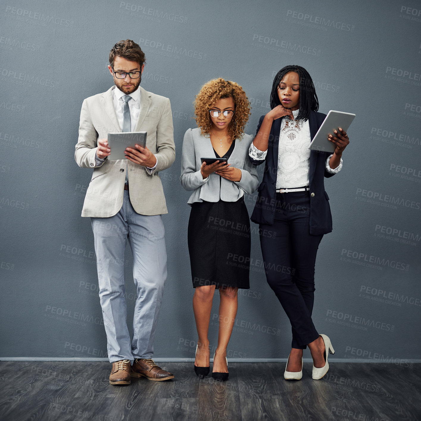Buy stock photo Full length shot of a group of businesspeople using digital tablets against a grey background