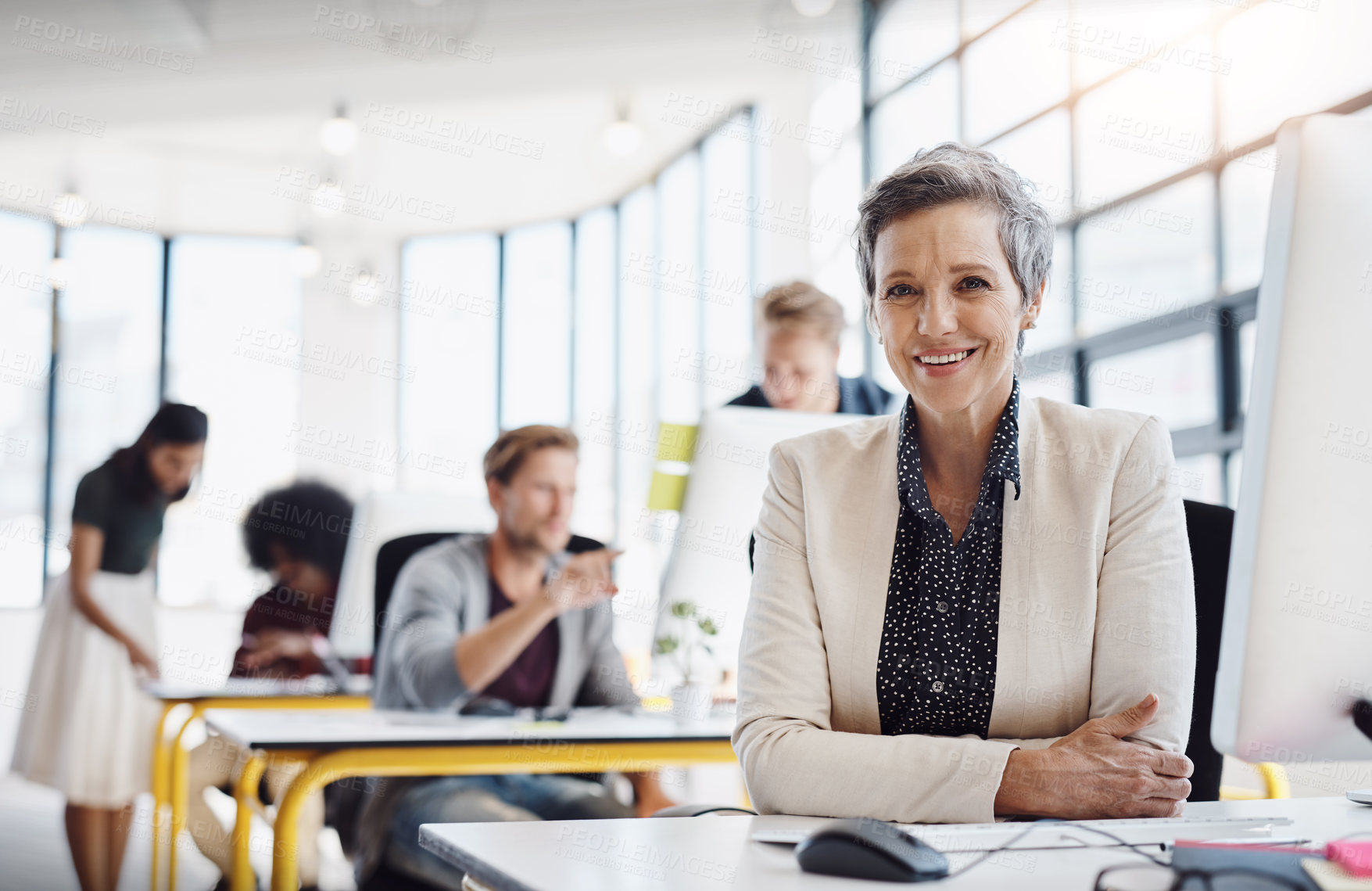 Buy stock photo Portrait of a happy designer posing in the office while her colleagues work in the background