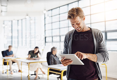Buy stock photo Shot of a happy designer using his tablet in the office while his colleagues work in the background