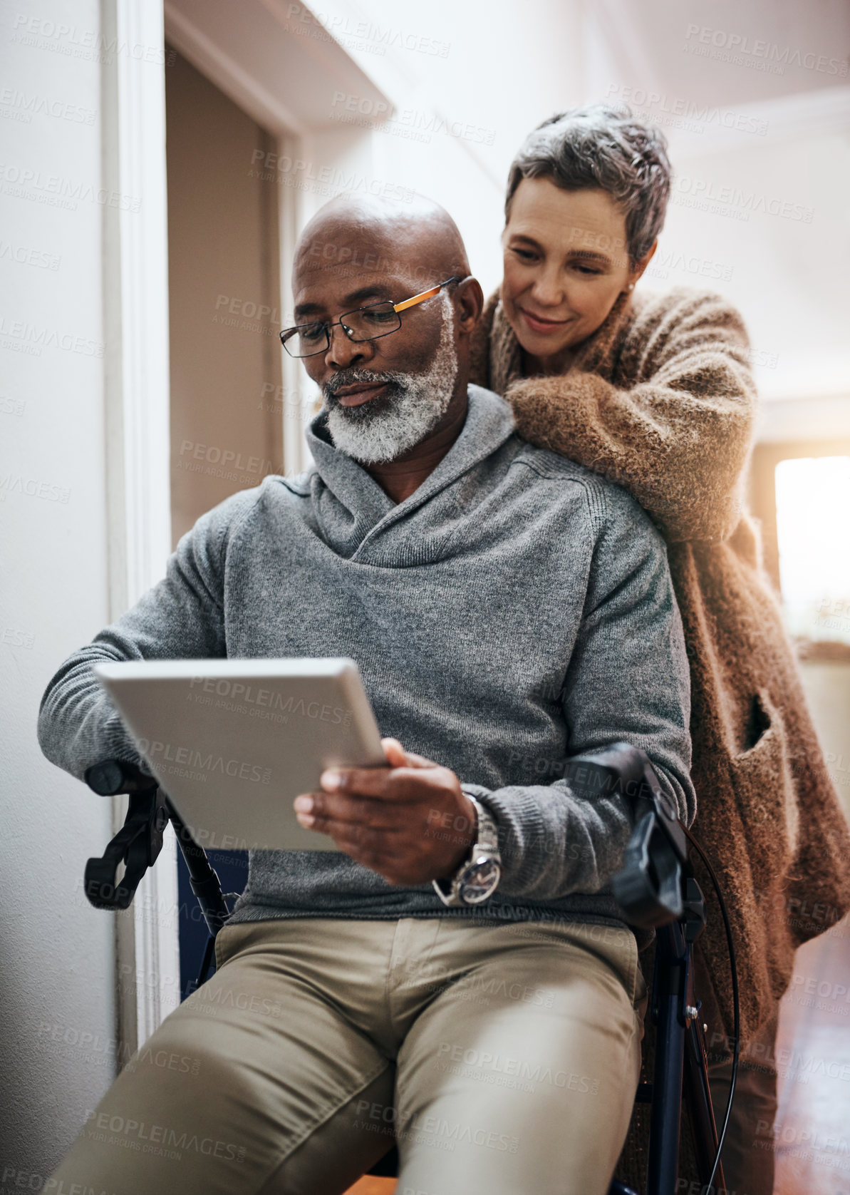 Buy stock photo Shot of an affectionate senior couple using a tablet at home with the man sitting in a wheelchair