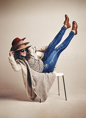 Buy stock photo Studio shot of a young woman sitting on a chair and wearing a pile of hats against a brown background