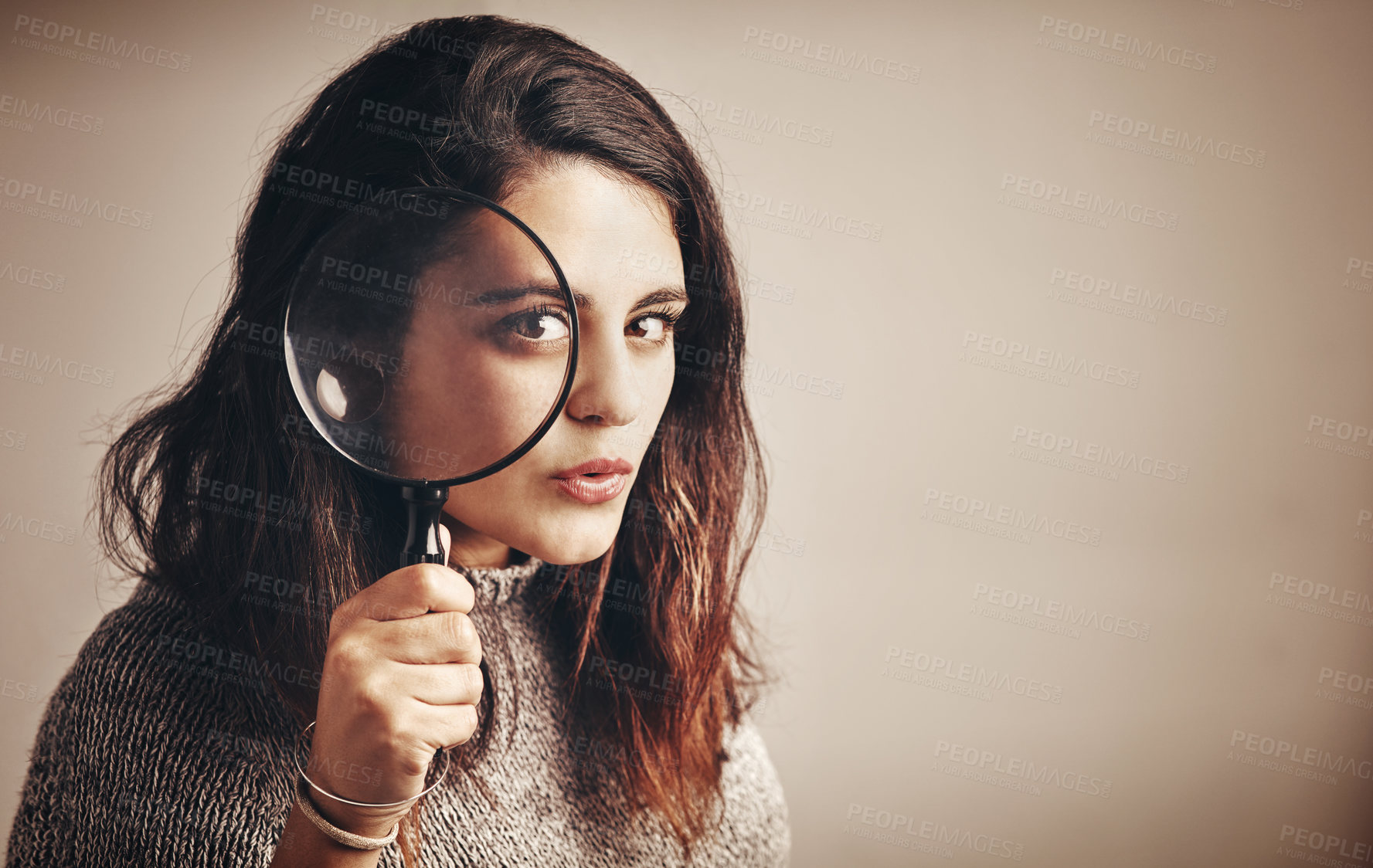 Buy stock photo Studio portrait of a young woman looking through a magnifying glass against a brown background