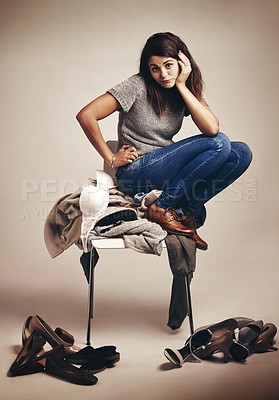 Buy stock photo Studio shot of a young woman trying to choose an outfit from a pile of clothes against a brown background