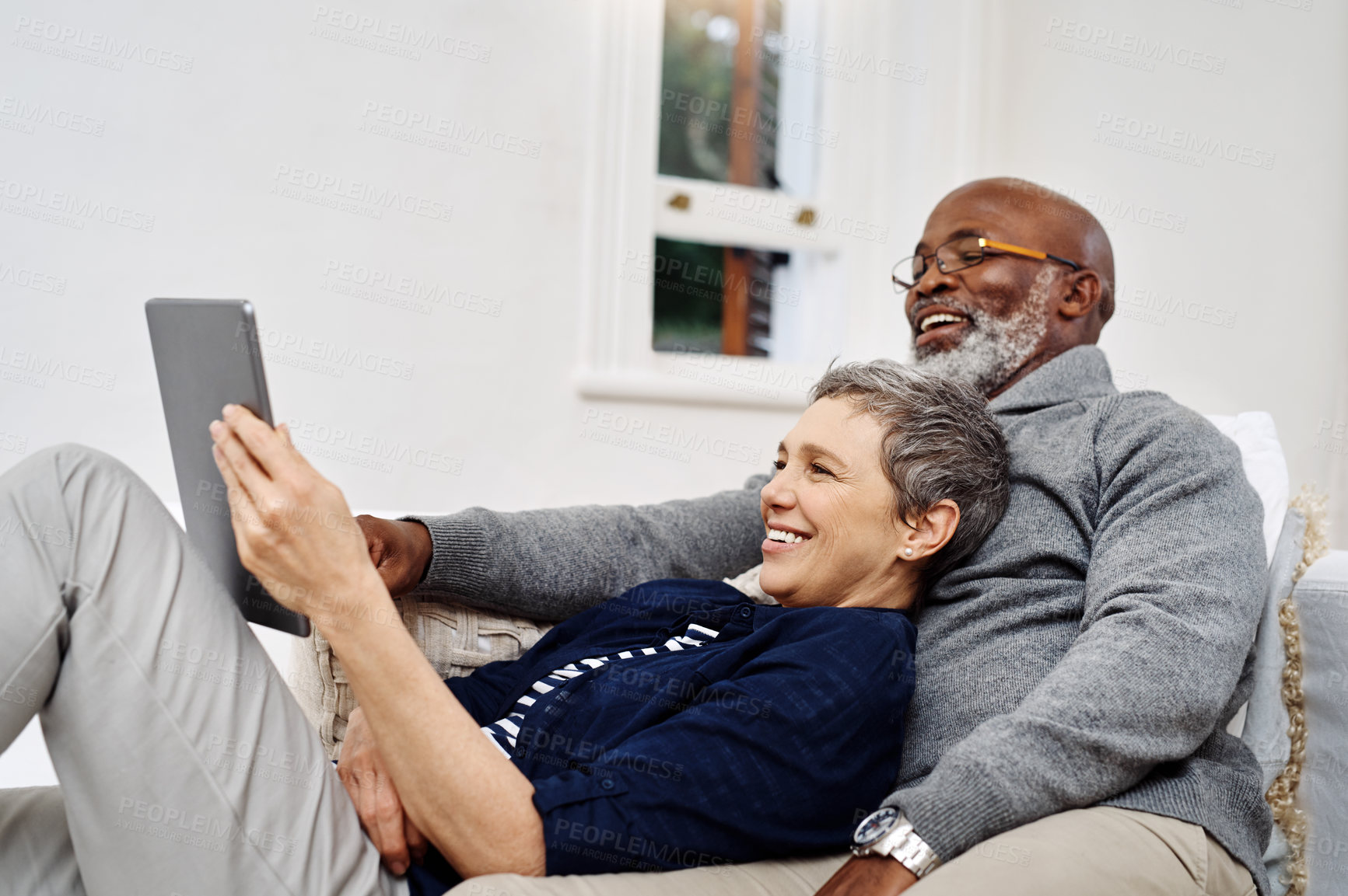 Buy stock photo Shot of an affectionate senior couple using a tablet while relaxing on the sofa at home