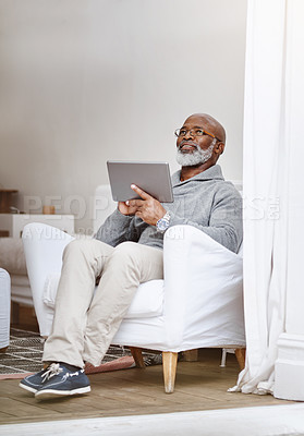 Buy stock photo Shot of a handsome senior man using his digital tablet while relaxing on a couch at home