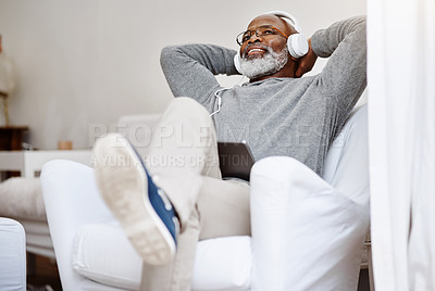 Buy stock photo Shot of a handsome senior man listening to music on a tablet while relaxing on a couch at home