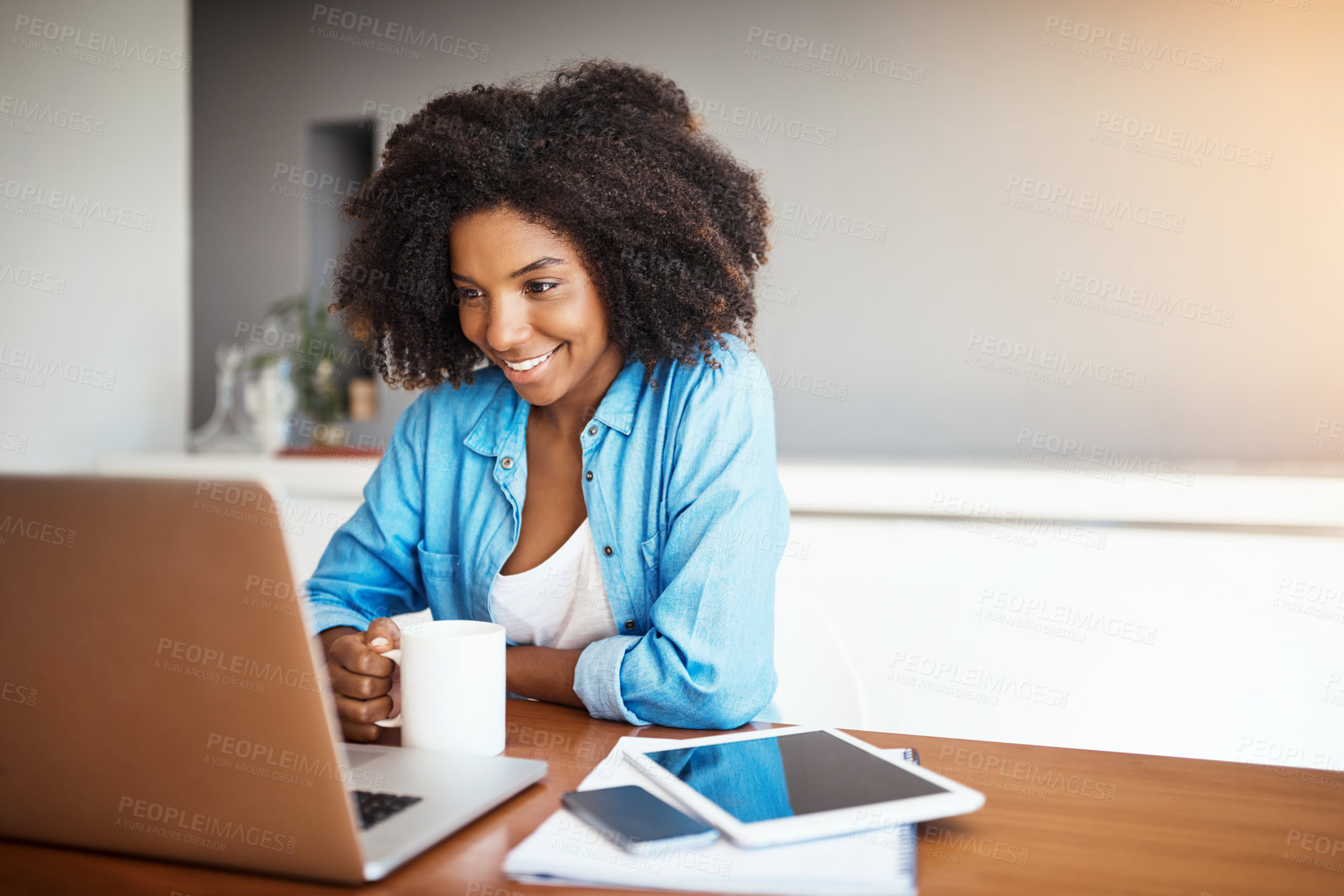 Buy stock photo Shot of an attractive young woman having a cup of coffee while working on her laptop at home