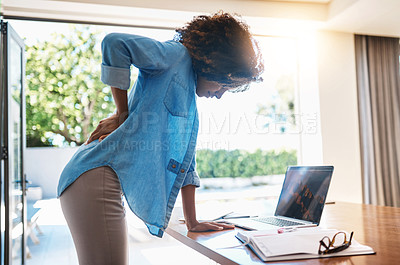 Buy stock photo Shot of a young woman experiencing back pain while working on her laptop at home