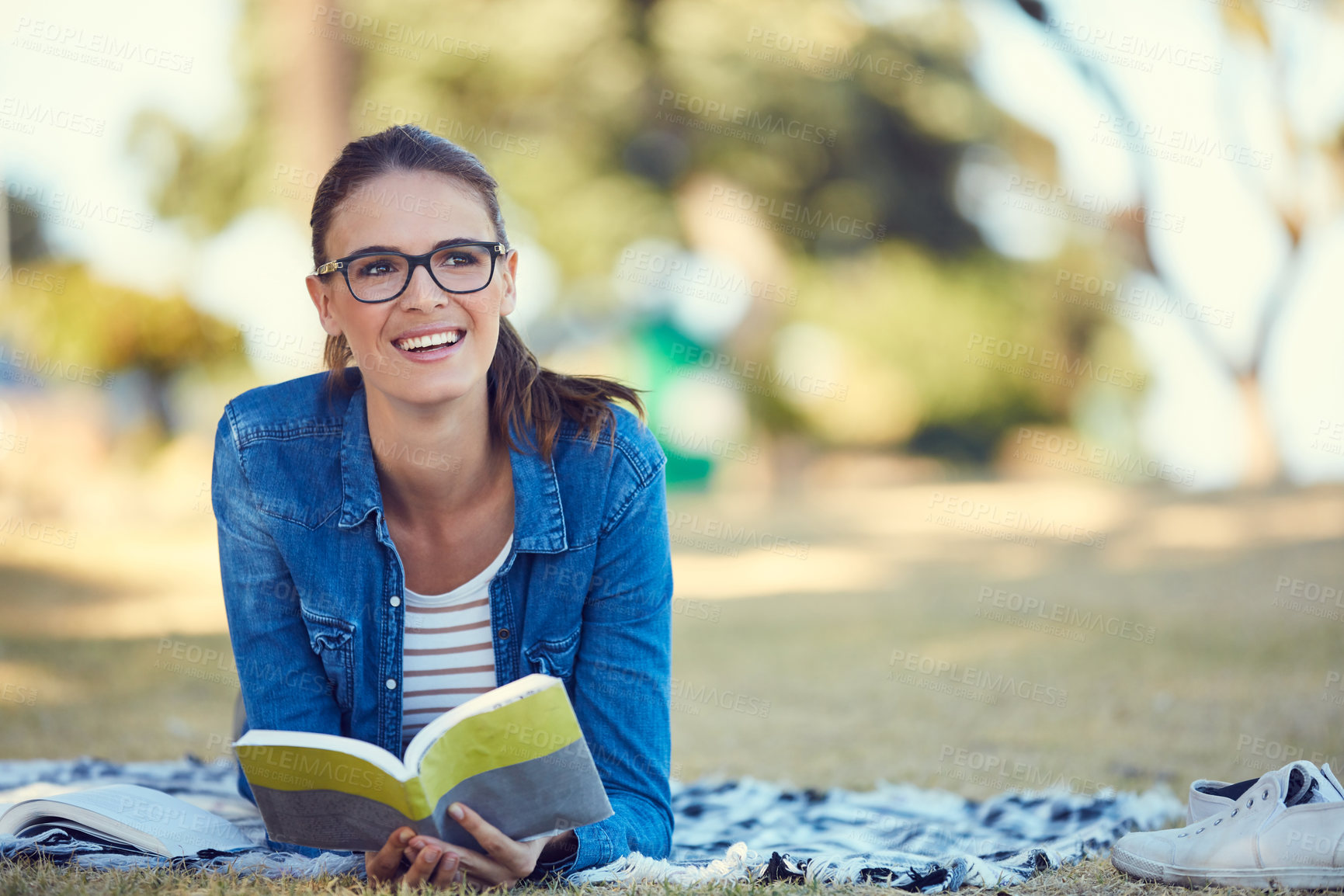 Buy stock photo Shot of an attractive young woman reading a book while relaxing in the park