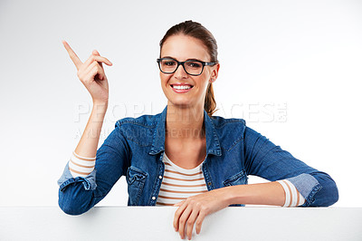 Buy stock photo Studio portrait of a young woman posing with a blank placard and pointing against a grey background