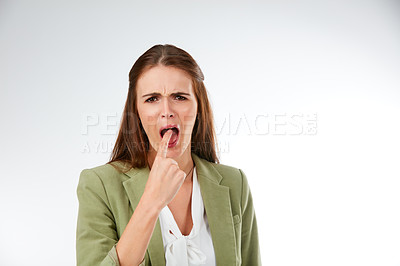 Buy stock photo Studio portrait of a young woman putting her finger in her mouth in disgust against a grey background