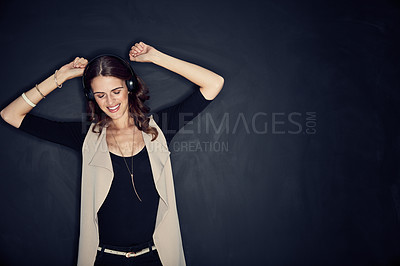 Buy stock photo Studio shot of an attractive young woman listening to music while posing against a dark background