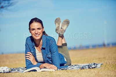 Buy stock photo Portrait of an attractive young woman reading a book while relaxing in the park