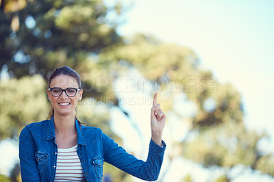 Buy stock photo Portrait of an attractive young woman standing in the park and pointing upwards